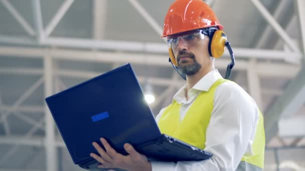 El empleado masculino de la fábrica está trabajando con su computadora portátil y echando un vistazo — Vídeos de Stock