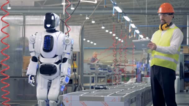 Fabrieksarbeider komt rond en op afstand geïnduceerde de robot te beginnen boren — Stockvideo