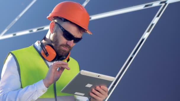 男性工人在他的平板上的类型, 而站在屋顶附近的太阳能电池板。4k. — 图库视频影像