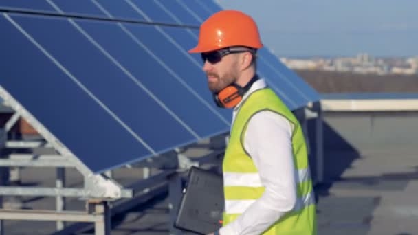 Hombre trabajador se vuelve a la cámara y sonríe, mientras que de pie en el techo cerca de paneles solares. 4K . — Vídeo de stock