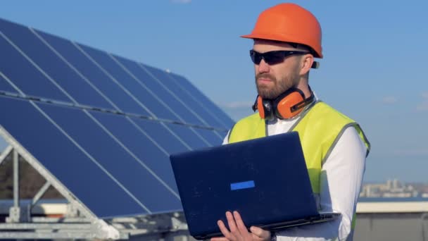 Trabalhador usa seu laptop, enquanto examina os painéis solares no telhado. 4K . — Vídeo de Stock