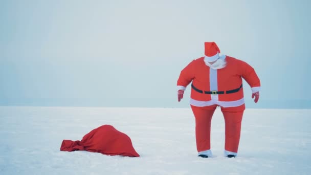 Papai Noel está pulando na neve ao lado de sua bolsa com presentes — Vídeo de Stock