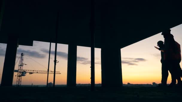 Stadsgebouw in uitvoering met ingenieurs die er langs lopen bij zonsondergang — Stockvideo