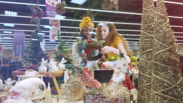 Chicas felices revisan decoraciones navideñas en una tienda . — Vídeos de Stock