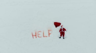 Karda yazan yardım işareti ve yanında bir kar meleği yapan Noel Baba.