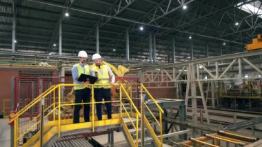 İki adam bir tuğla fabrikasında çalışıyor, makineleri kontrol ediyorlar. Fabrikadaki profesyonel fabrika işçileri.