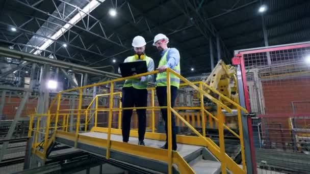 Engenheiros trabalham com um laptop em uma fábrica industrial moderna. Trabalhadores de fábrica profissionais nas instalações da fábrica . — Vídeo de Stock