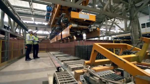 İki mühendis bir tuğla fabrikasında çalışan bir yükleyiciyi kontrol ediyor. Fabrikadaki profesyonel fabrika işçileri. — Stok video