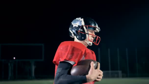 Un giocatore di football americano cammina su un campo, tenendo una palla, vista laterale . — Video Stock
