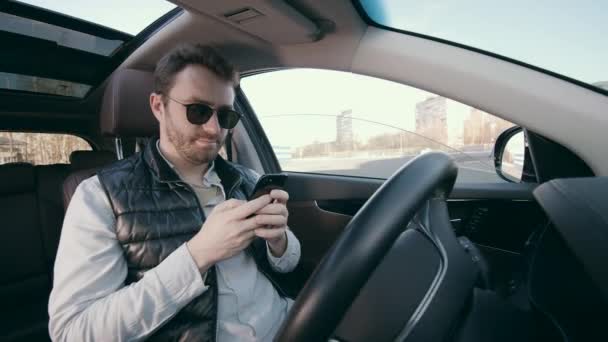 Conductor masculino con un teléfono inteligente está sentado en un coche automático — Vídeos de Stock