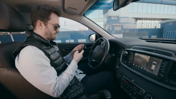 Muž si prohlíží smartphone, zatímco se jeho auto pohybuje. — Stock video