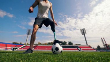 Futbol sahası ve top oynayan protez bacaklı bir adam.