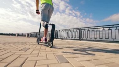 Yapay bacaklı engelli adam yavaş çekimde scooter kullanıyor.