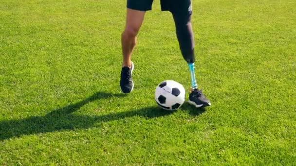 Muž s bionickou nohou kape míčem na zelený trávník. — Stock video
