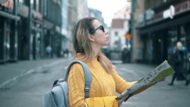 Una señora con un mapa está mirando alrededor de una calle de la ciudad — Vídeo de stock