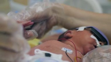 Tek kullanımlık eldivendeki bir el, bir bebeğin elini tutuyor.