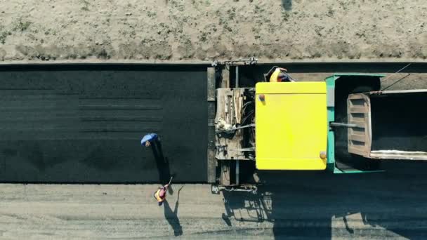 Asphalt paver машина на місці будівництва дороги. Дорожники викидають бітум з машин. — стокове відео
