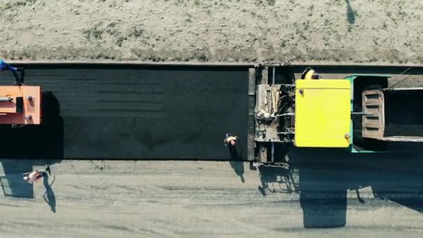 Asphalt paver машина на місці будівництва дороги. Верхній вид дорожніх машин, що прокладають асфальт. — стокове відео