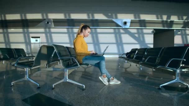 Eine Frau bedient einen Laptop, während sie in der Abflughalle sitzt — Stockvideo