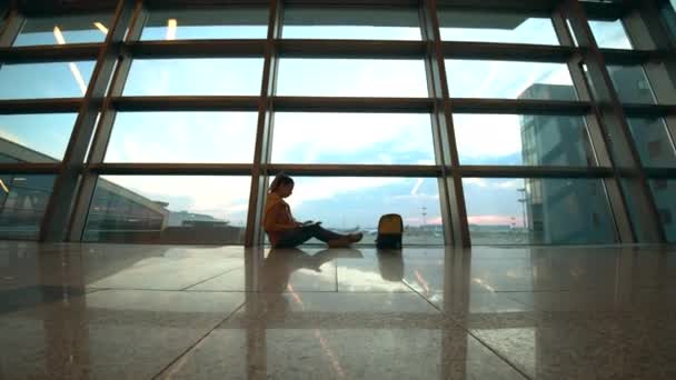 Eine Frau mit Laptop sitzt auf dem Boden der Abflughalle — Stockvideo