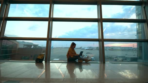 한 여성 이 컴퓨터를 가지고 출국 라운지 바닥에 앉아 있습니다 — 비디오