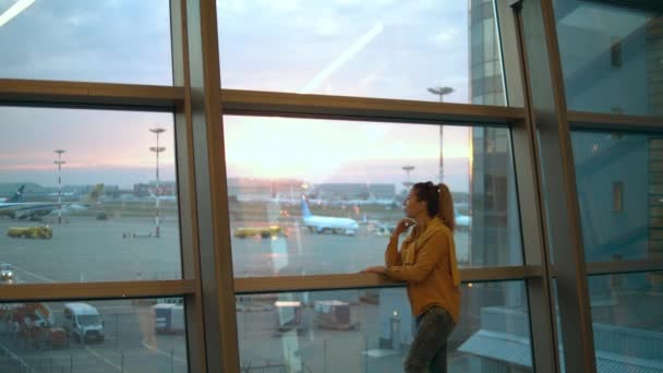 Женщина подходит к окну аэропорта и наблюдает за площадкой — стоковое видео