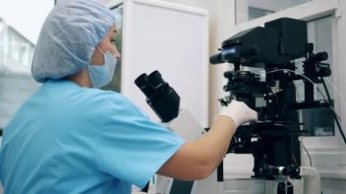 Kadın uzman, tıbbi laboratuvar çalışanı mikroskop altında madde gözlemliyor.