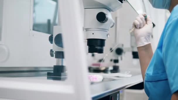 Trabajador de laboratorio de química está llenando un tubo con sustancia bajo un microscopio — Vídeo de stock