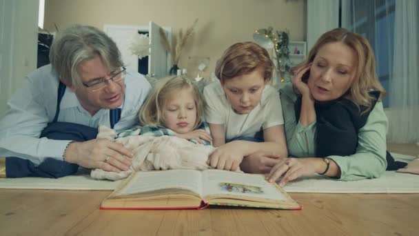 Barnen läser en bok med sin mormor och morfar. — Stockvideo