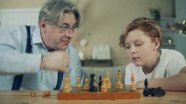 Yaşlı adam torununa satranç oynamayı öğretiyor.