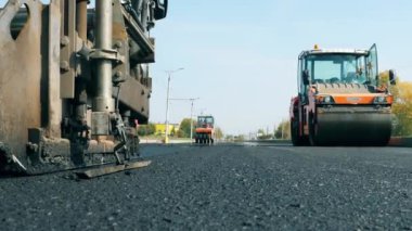 Yol boyunca uzanan bitum yayıcılarının ön görüntüsü. Yol yapımında çalışan inşaat işçileri