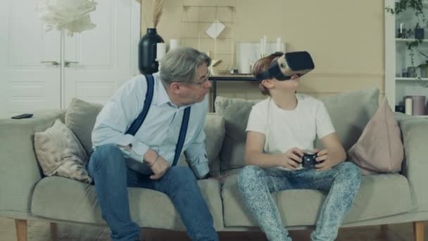 Oude man observeert zijn kleinkind terwijl hij een Vr-wedstrijd speelt. — Stockvideo