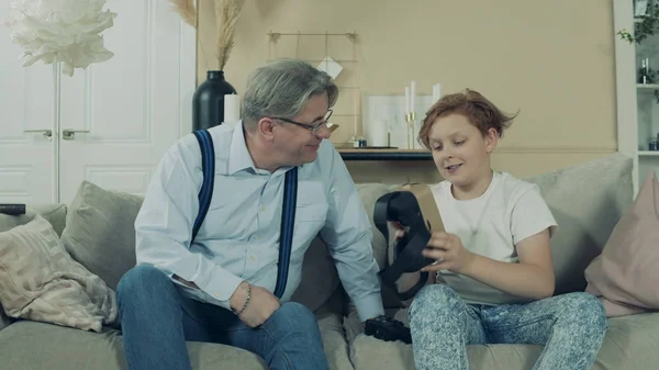 Genç çocuk dedesine VR gözlüklerini gösteriyor.