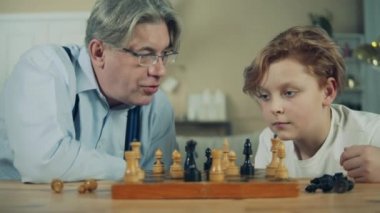 Yaşlı adam ve torunu satranç taşlarına yakından bakıyorlar.