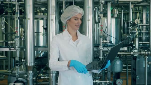 Lavoratrice con un computer portatile è in piedi in un'unità di fabbrica — Video Stock