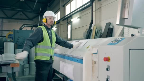 Работник мужского пола управляет машиной, обрабатывающей металлический лист — стоковое видео