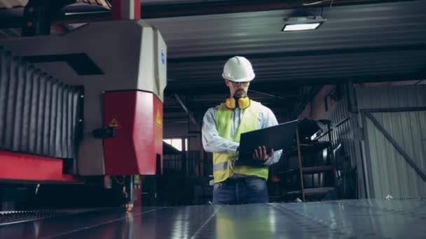 Fabrieksmedewerker kijkt naar laserapparatuur die metaal snijdt. Professionele zware industrie ingenieur. — Stockvideo