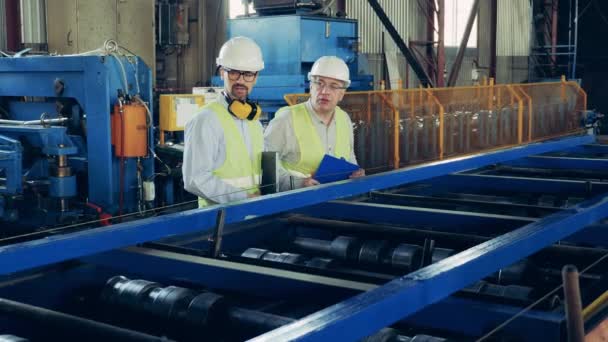 Ingenieros masculinos en fábrica industrial. Dos expertos están observando un transportador rodante — Vídeos de Stock