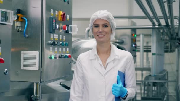 Woman in uniform smiles, while standing in a dairy factory room. — Stockvideo