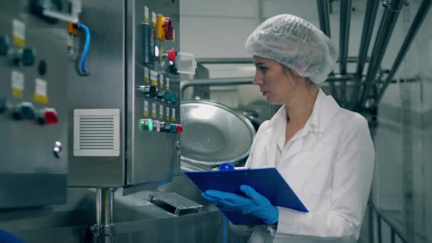 Trabalhadora controla a qualidade do equipamento de produção. Uma mulher verifica a máquina em uma fábrica de laticínios . — Vídeo de Stock