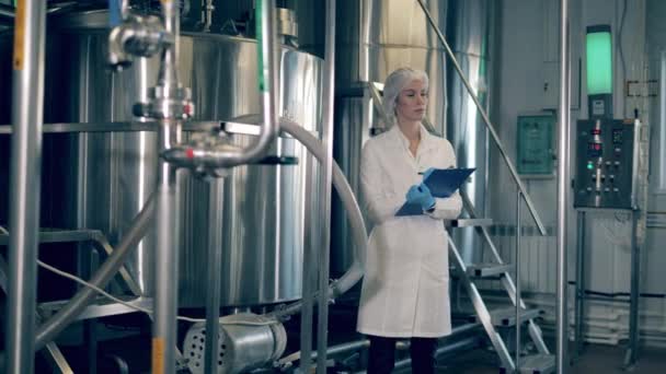 Female worker controls the quality of production equipment. Factory worker writes notes while checking equipment. — Stockvideo