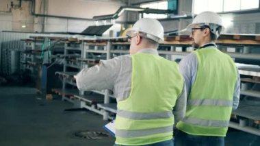 İnşaat malzemeleri ve iki işçinin yürüdüğü fabrika ünitesi. Endüstriyel fabrikada erkek mühendisler.