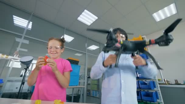 Twee kinderen spelen met een quadcopter, drone in een laboratorium. — Stockvideo