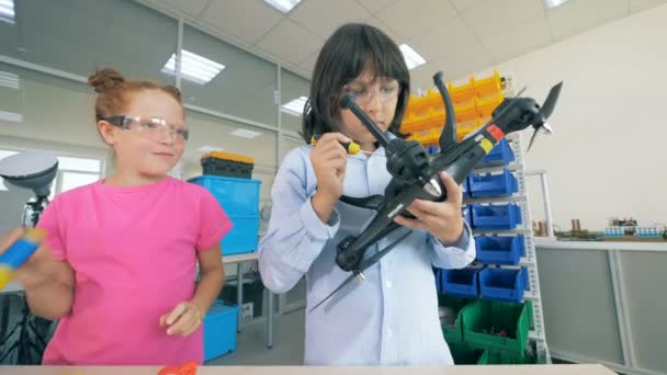 Ein Junge und ein Mädchen reparieren spöttisch einen Quadrocopter. — Stockvideo