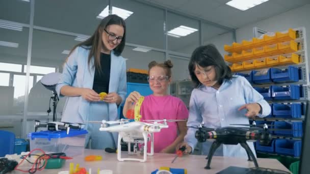 Sala de jogos de engenharia com adolescentes trabalhando em quadricópteros sob supervisão de trabalhadores de laboratório — Vídeo de Stock