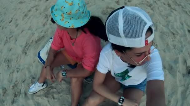 Duas senhoras estão filmando-se enquanto estão sentadas na areia — Vídeo de Stock