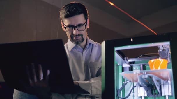 Man met laptop checkt werkende 3D printer. 3d printing industrie ingenieur werkt in 3d printing lab. — Stockvideo