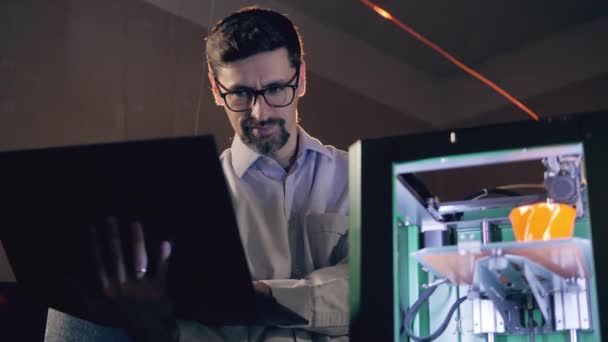 Man with laptop checks working 3D printer. 3d printing industry engineer works in 3d printing lab. — 비디오