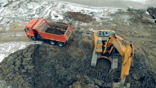 Kazı makineleri ve kamyonlarla çalışan bir inşaat alanının üstünden hava görüntüsü. Bir yükleyici kamyona taş ve kum koyar.. — Stok video