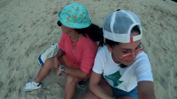 Meninas se sentam em uma praia, se divertindo . — Vídeo de Stock